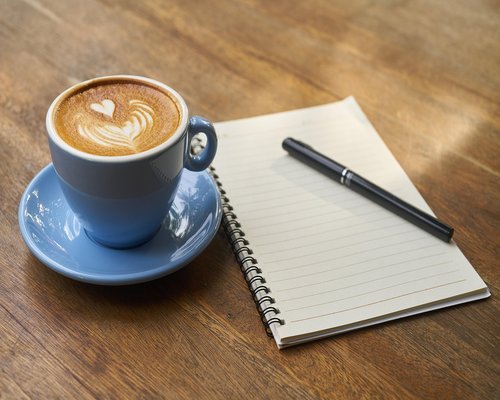 Coffee cup and notebook on a table with bright sunlight